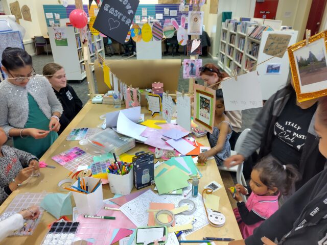 Image of table and craft material with people gathered around writting